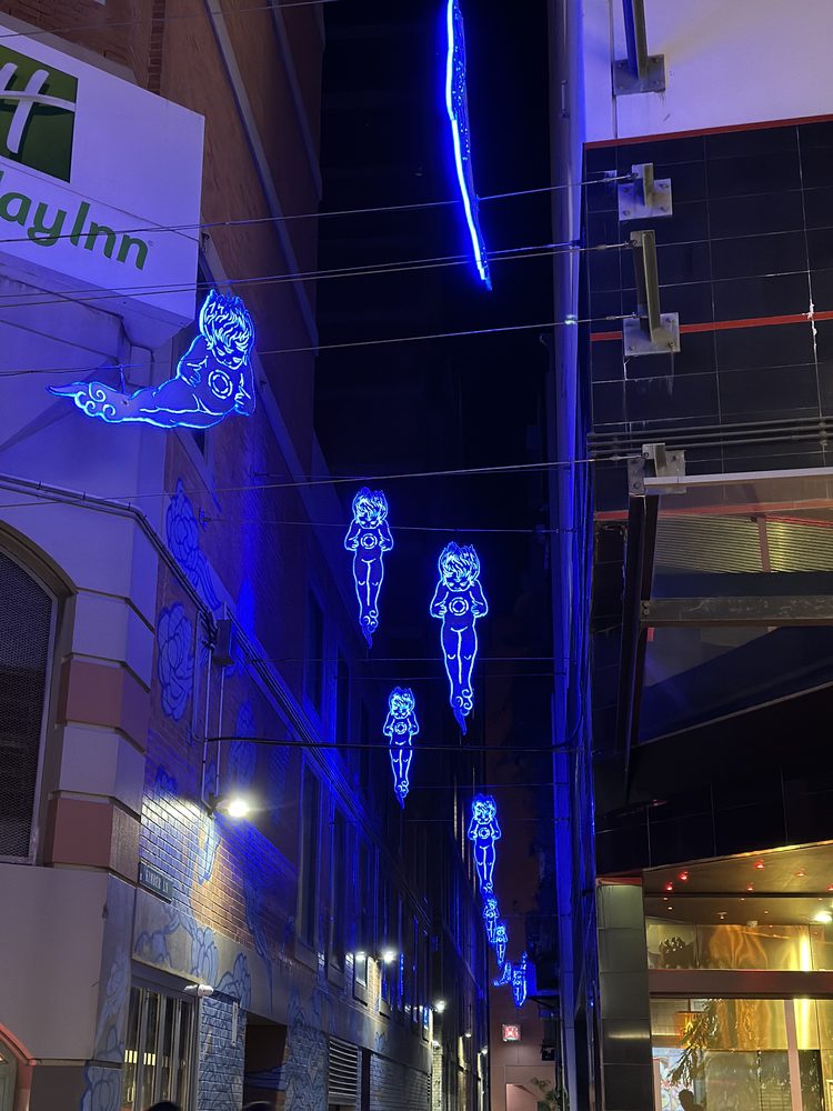 Blue neon cherub light sculptures above a Chinatown laneway